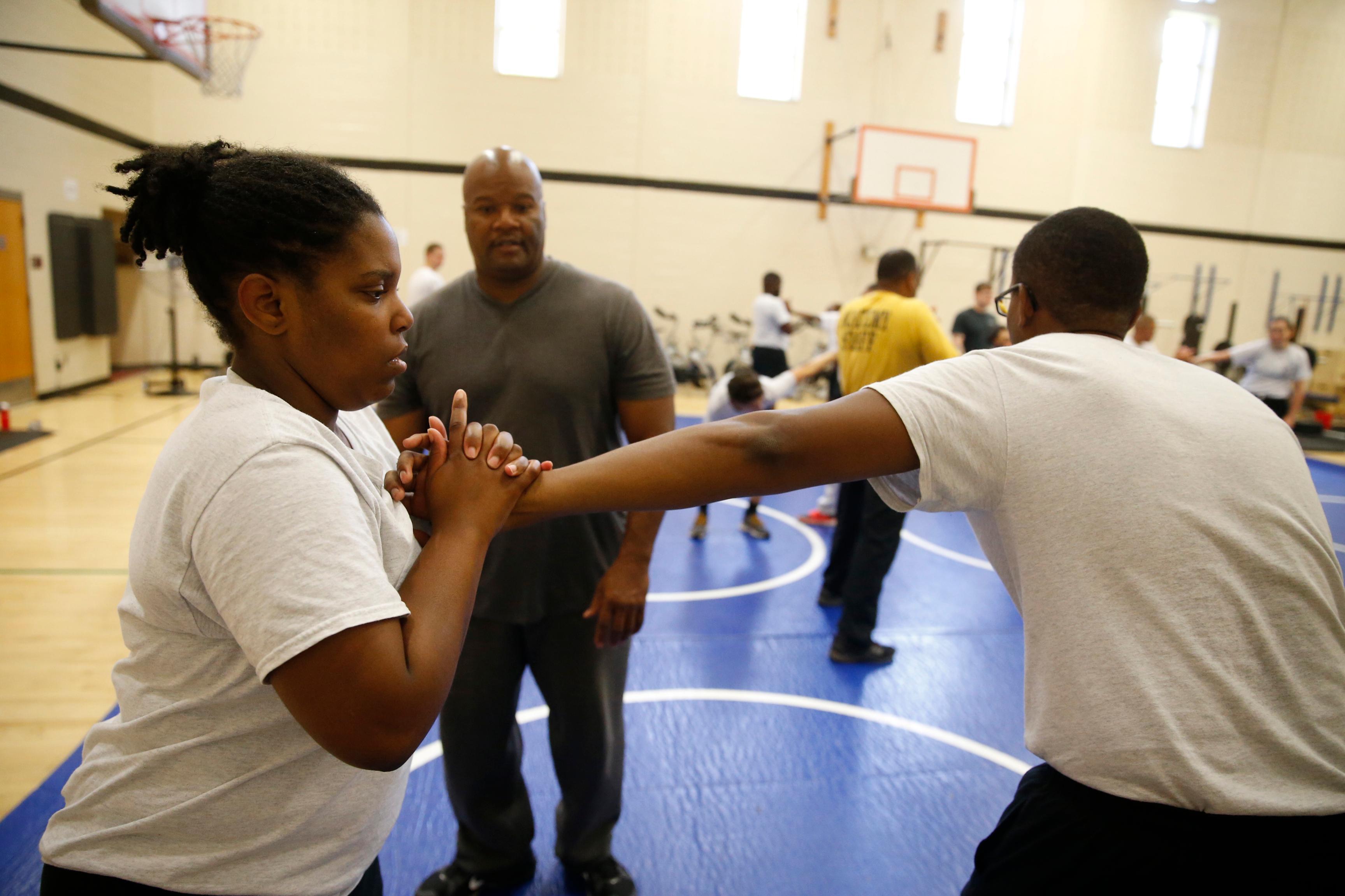 Academy recruit Chelsea West (right) practices  a wrist lock on a fellow recruit at the direction of Deputy Michael Robertson (center). 